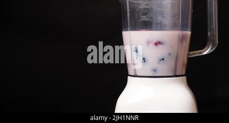 Milchshake in einer Schüssel mit einem Mixer aus Milch, Erdbeeren und Brombeeren auf schwarzem Hintergrund, ein Ort für Text Stockfoto
