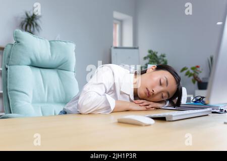 Die junge asiatische Geschäftsfrau schlief am Schreibtisch auf ihren Händen im Büro ein, müde, routinemäßige, langweilige Arbeit, braucht eine Pause. Stockfoto
