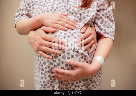 Beschnittenes Bild einer schönen Schwangeren und ihres hübschen Mannes, der sich am Bauch umarmt Stockfoto