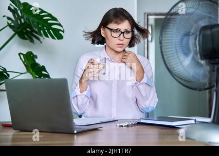 Frau mittleren Alters, die an Hitze leidet, überhitzt, durch Ventilator und Ventilator gekühlt Stockfoto