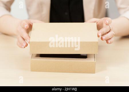 Frau öffnet Box mit neuem Paket, Nahaufnahme Stockfoto