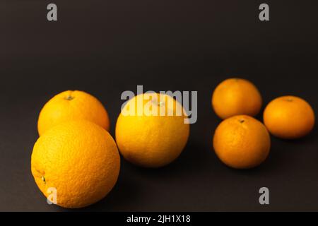 Frische Orangen nahe verschwommener Mandarinen auf schwarzem Hintergrund Stockfoto