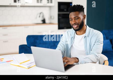 Ein Mann aus der Mitte des Erwachsenen, der in seinem Heimbüro arbeitet und einen Laptop für die Kommunikation mit Kunden oder Kollegen verwendet. Lächelnder Kerl, der lächelnd auf dem Computerbildschirm zusieht Stockfoto