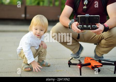 Vater und Sohn beobachten und steuern eine Drohne. Netter kleiner Junge, der seinem Vater hilft, eine Drohne per Fernbedienung zu bedienen. Familienurlaub. Stockfoto