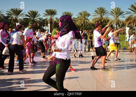 Lustige arabische Frau, die Hijab trägt, macht ein paar Tanzbewegungen aus, während die Menge einem Lehrer bei einem Color Walk in Dubai, Vereinigte Arabische Emirate, folgt. Stockfoto