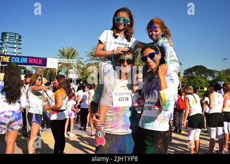 Fröhliche, lächelnde Familie posiert für ein Foto beim Color Walk in Dubai, Vereinigte Arabische Emirate. Eltern haben beide Töchter auf Huckepack. Unterhaltsame Outdoor-Veranstaltung. Stockfoto