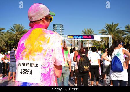 Nahaufnahme eines Rennfahrers auf dem Rücken eines Teilnehmers, einem jungen weißen Mann, der mit farbigem Pulver bedeckt war, bei einem Color Walk in Dubai, Vereinigte Arabische Emirate. Stockfoto