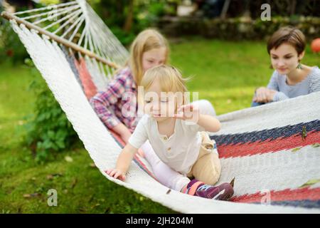 Glücklicher Kleinkind Junge und seine Teenager-Schwestern entspannen in Hängematte an schönen Sommertag. Nette Kinder, die Spaß im Sommerpark haben. Familienfreizeitangebot im summ Stockfoto