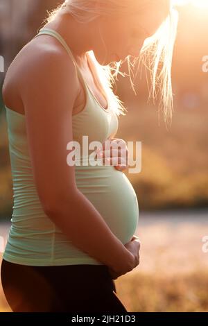 Profil einer Schwangeren, die ihren Bauch umarmt Stockfoto