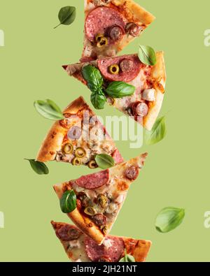 Fliegende Nahrung. Pizzascheiben mit Käse, Wurst, Salami, Oliven und Basilikum in Levitation auf olivem Hintergrund. Vertikale Ausrichtung Stockfoto