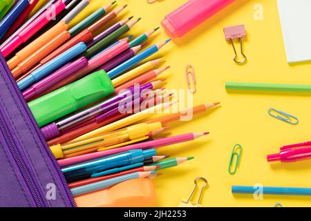 Stellen Sie sich verschiedene Büromaterialien und Plastikutensilien, Bleistifte, Buntstifte auf gelbem Hintergrund vor Stockfoto
