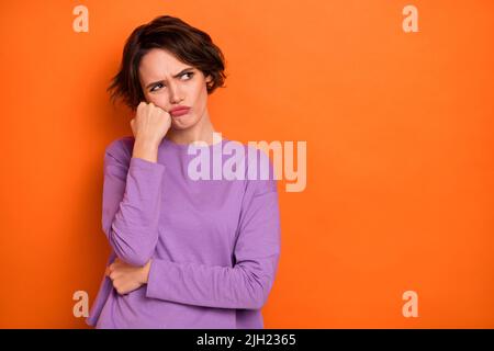 Foto von unzufriedene launische Person Hand berühren Wange suchen leeren Raum auf orangen Hintergrund isoliert Stockfoto