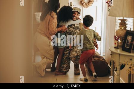 Herzerwärmende militärische Heimkehr. Glücklicher Soldat, der sich nach seinem Militärdienst mit seiner Frau und seinen Kindern wiedervereinigt. Fröhlicher Militärangehöriger umarmt seine Familie Stockfoto