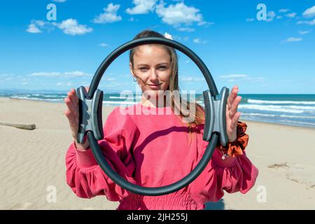 Junge Frau zeigt Pilates Reifen am Strand Stockfoto