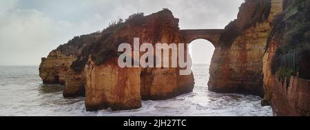 Ein Bogen verbindet einen der Felsen mit der Festlandlandschaft bei bewölktem Wetter Stockfoto