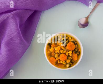 Draufsicht, Nahaufnahme der Gemüseeintopf-Schüssel, isoliert auf hellblauem Hintergrund. Frischer, hausgemachter, gesunder veganer Eintopf mit Karotten, Mais, Spinat, Brokkoli geschmort. Stockfoto