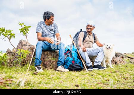 Wanderer mittleren Alters mit Hund oder Haustier, die sich während des Trekkings unterhalten, während sie auf dem Hügel sitzen - Vorstellung von Reisenden, Glück und Kommunikation. Stockfoto