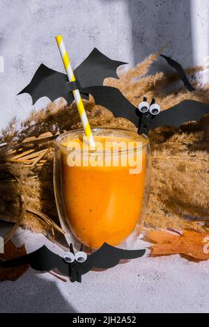 Kürbis-Smoothie gewürzter Latte. Herbstgetränke für Halloween-Dekorationen mit Fledermaus auf Stroh. Feiertagsgetränk Herbstkaffee mit würzigem Kürbisgeschmack der Saison Stockfoto