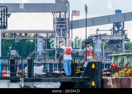 NEW ORLEANS, LA, USA - 11. JULI 2022: Schlepper-Deck-Crew bei der Arbeit neben einem Lastkahn auf dem Mississippi River mit einem Getreideaufzug im Hintergrund Stockfoto