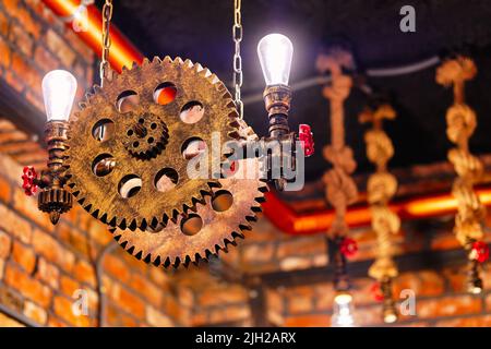 Steampunk Design-Element im architektonischen Stil des Innenraums. Lampen, die auf Zahnrädern mit Eisenzahnrädern befestigt sind, beleuchteten Geräte, die in Innenräumen hängen Stockfoto