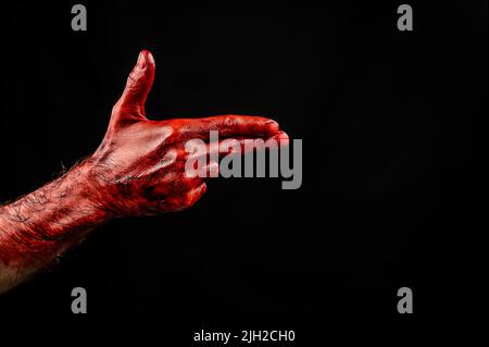 Blutige männliche Hand zeigt eine Waffe vor schwarzem Hintergrund. Stockfoto