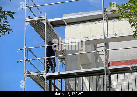 Renovierung einer Wärmedämmung an einem Wohngebäude Arbeiter entfernt den alten Putz an einer Hausfassade, Außenwand, Gerüst, Fassade, Außenverkleidung, Isolierung. Renovierung, Vollwärmeschutz, Baustelle, Wohnbau, Wohngebäude, Eigentumswohnung, Wohnungsbau, Bauindustrie, Bauarbeiter, Bauboom, Bauindustrie. Stockfoto