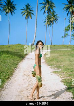 Frau, die Ananas auf einem Sandweg trägt. Playa Rincon, Las Galleras. Samana-Halbinsel, Dominikanische Republik Stockfoto