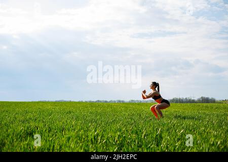 Mädchen Athletin hockt in der Natur, Übungen für das Gesäß Stockfoto