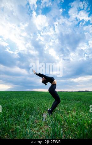 Eine schöne Brünette auf einem grünen Rasen führt akrobatische Elemente auf Stockfoto