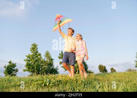 Bruder und Schwester mit einem Drachen, die auf dem grünen Gras laufen. Stockfoto