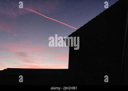 Lila und rosa Sonnenuntergang Himmel hinter einer Silhouette eines Hauses. Stockfoto