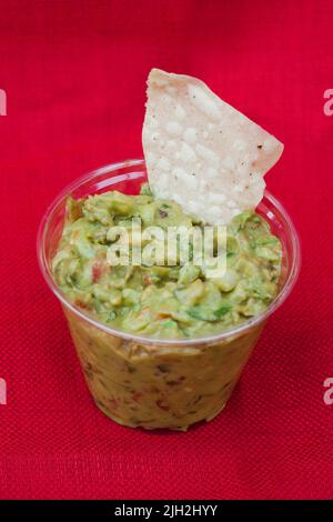 Eine Tasse Guacamole in einem mexikanischen Restaurant in einer klaren Tasse auf hellrotem Hintergrund. Stockfoto