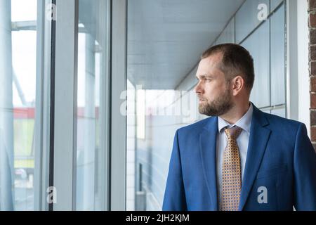 Ein intelligenter, ernsthafter, selbstbewusster arabischer Geschäftsmann, der aus dem Fenster auf die Straße blickt. Porträt eines gutaussehenden Geschäftsmannes mittleren Alters in einem Anzug. Die Conce Stockfoto