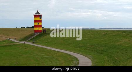 Süßer deutscher Leuchtturm in rot und gelb. Er wurde 1891 gebaut und ist 11 Meter hoch. Es ist bekannt als der Leuchtturm von Pilsum. Er steht auf einem Deich. Darunter Stockfoto