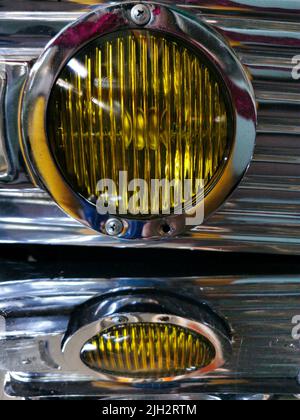 Nahaufnahme von gelben runden Scheinwerfern eines Retro-Autos auf glänzendem silbernen Metall. Stockfoto