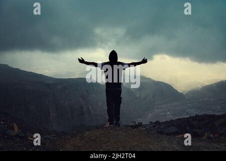 Der Mann hob die Hände und genoss die Aussicht vom Gipfel des Berges in Jabel Jais, Ras Al Khaimah, Vereinigte Arabische Emirate Stockfoto