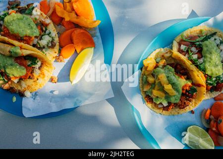 Zwei blaue Teller auf dem Außentisch, jeweils mit zwei Tacos, Limettenkeil und Karottenescabeche Stockfoto
