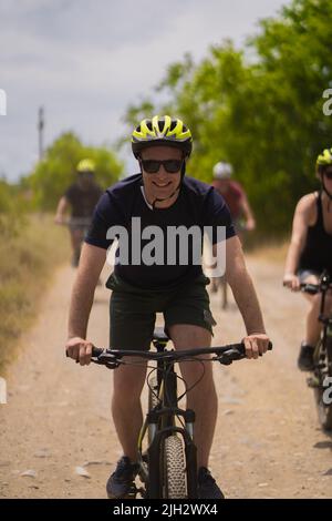 Porträt eines blonden Mannes, der lächelt und mit dem Fahrrad fährt, während er den Tag genießt Stockfoto