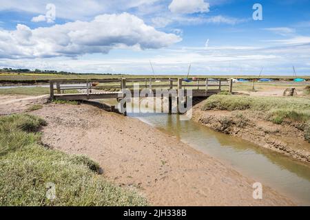 Eine Holzbrücke überspannt bei Ebbe einen Wasserkanal bei Blakeney an der Nordnorfolk-Küste. Stockfoto