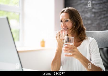 Nahaufnahme des Lächelnden jungen Frau die Pille im Glas Wasser auf Schreibtisch Stockfoto