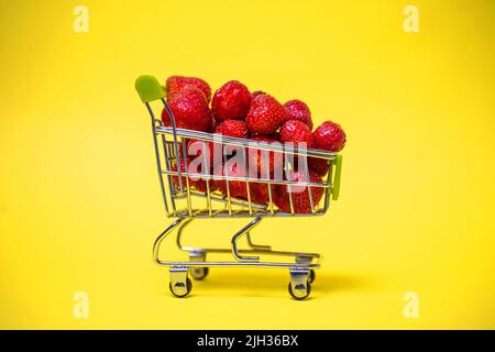 Ein Supermarkt-Wagen voller roter Erdbeeren auf gelbem Hintergrund. Stockfoto