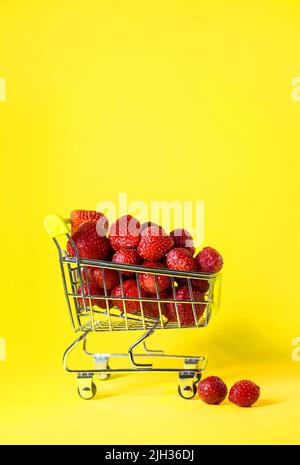 Ein Supermarkt-Wagen voller roter Erdbeeren auf gelbem Hintergrund. Stockfoto