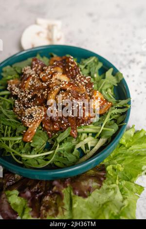 Warmer Salat mit Pilzen und Rucola in Nahaufnahme auf hellem Hintergrund. Stockfoto