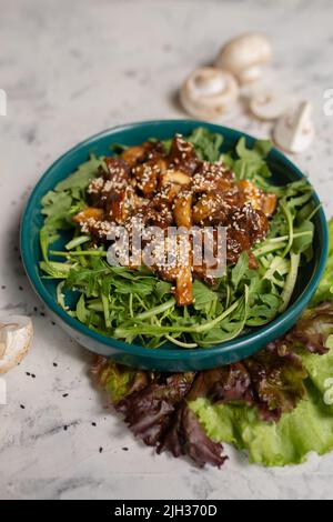 Warmer Salat mit Pilzen und Rucola in Nahaufnahme auf hellem Hintergrund. Stockfoto