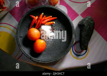 Sambal tomat ist ein beliebtes indonesisches Gewürz aus roten Chilischoten, Tomaten, Garnelenpaste, Zucker und Salz in traditionellem Mörser und Stößel Stockfoto