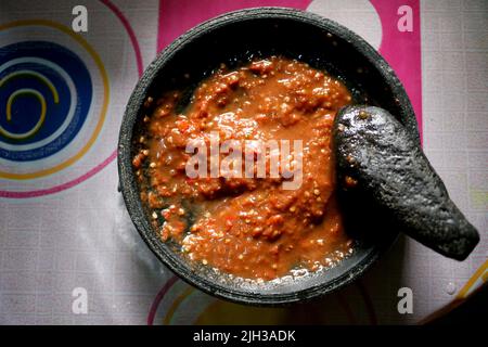 Sambal tomat ist ein beliebtes indonesisches Gewürz aus roten Chilischoten, Tomaten, Garnelenpaste, Zucker und Salz in traditionellem Mörser und Stößel Stockfoto