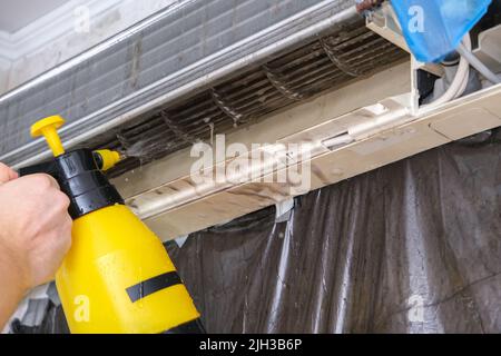 Ein Mann wäscht einen speziellen Schaum ab, um Klimaanlagen mit einem Wasserstrahl unter Druck zu reinigen. Wartung des geteilten Systems. Stockfoto