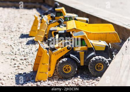 Gelbe Kinder-Tonka-Lastwagen parkten in einer Reihe in einer trockenen Kiesgrube, bereit zum Spielen beim Bauen, Graben und Bau neuer Häuser und Gebäude Stockfoto