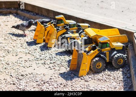 Gelbe Kinder-Tonka-Lastwagen parkten in einer Reihe in einer trockenen Kiesgrube, bereit zum Spielen beim Bauen, Graben und Bau neuer Häuser und Gebäude Stockfoto