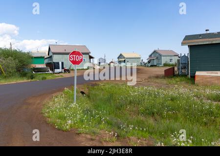 Stoppschild und Häuser entlang der Feldstraße der nördlichen indigenen Gemeinschaft Deline im Sommer, Northwest Territories, Kanada. Stockfoto